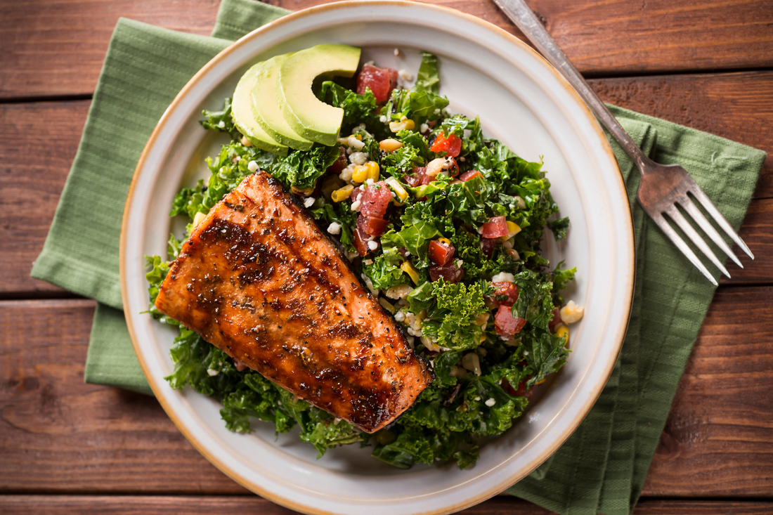 Berry-glazed salmon served on a bed of kale salad with avocado slices, highlighting its nutritious and anti-inflammatory ingredients.