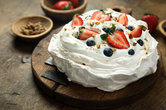 A delicious Low Sugar Berry Pavlova topped with Greek yoghurt, strawberries, and blueberries, served on a rustic wooden board.