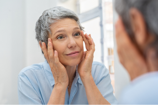 Older woman looking at herself in the mirror and touching her skin.