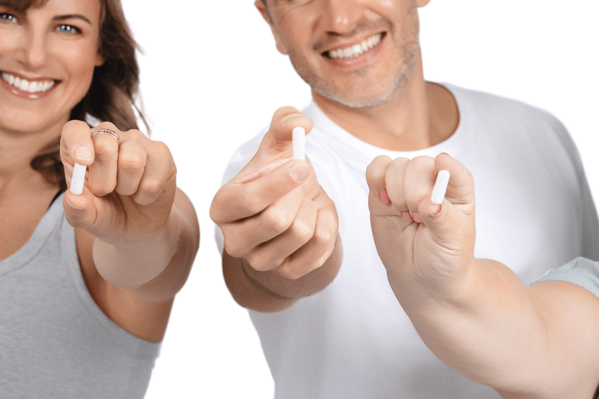 Three smiling people holding white supplement capsules towards the camera.