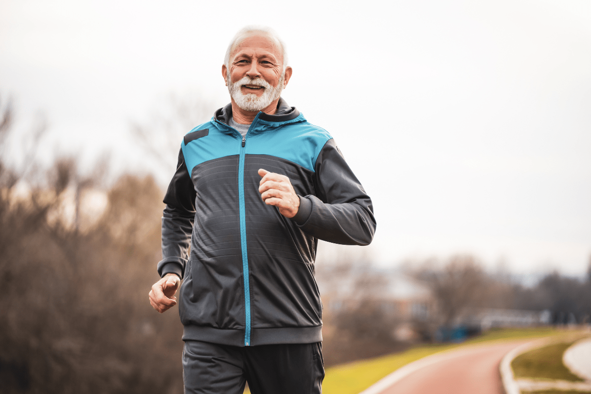 An older man in a tracksuit jogging outdoors, smiling and staying active.