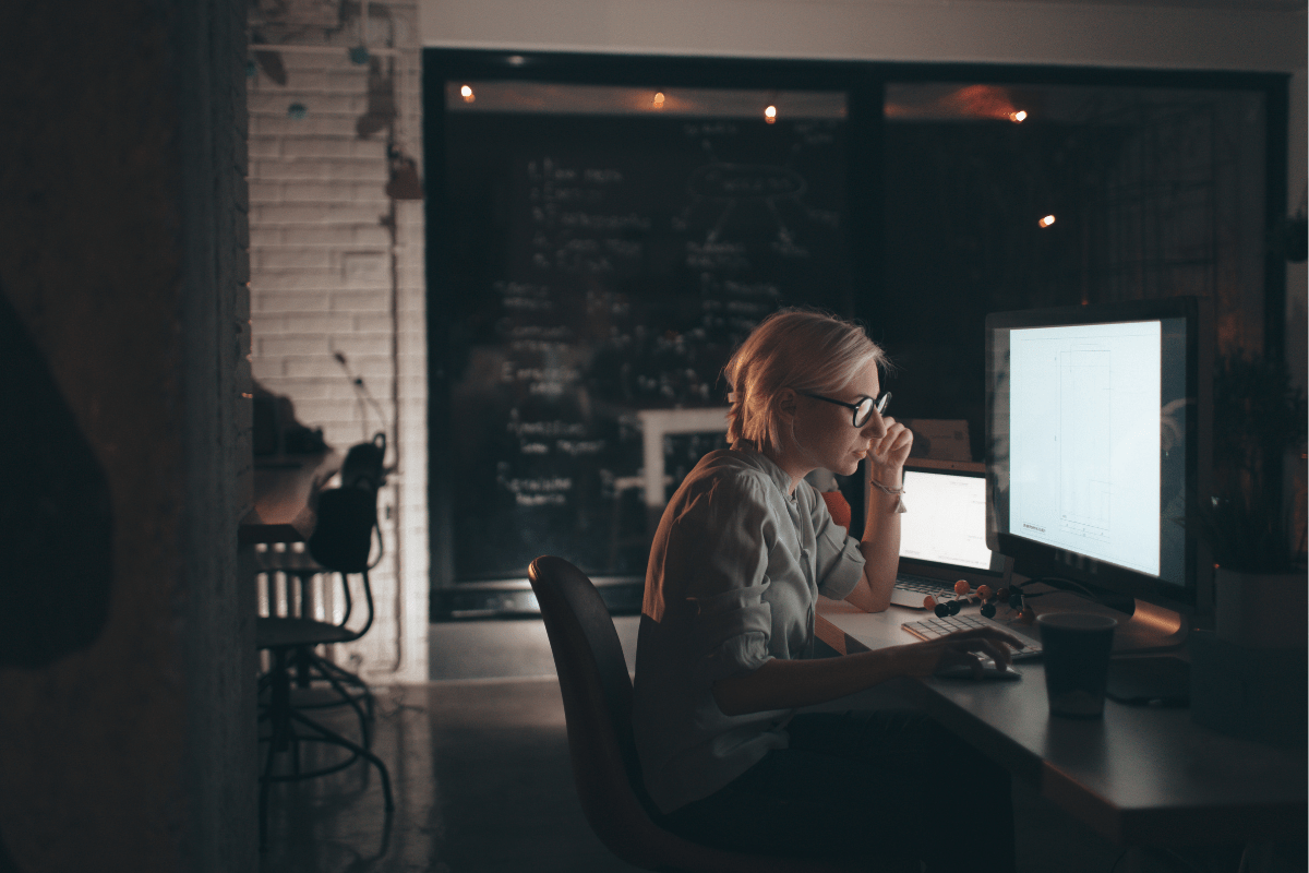 Person working late at night in a dimly lit office, focused on a computer screen.