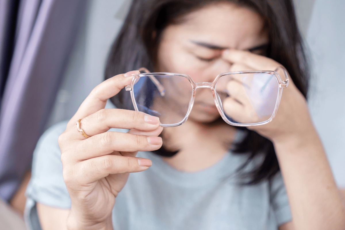 A woman holding her glasses while rubbing her tired eyes.