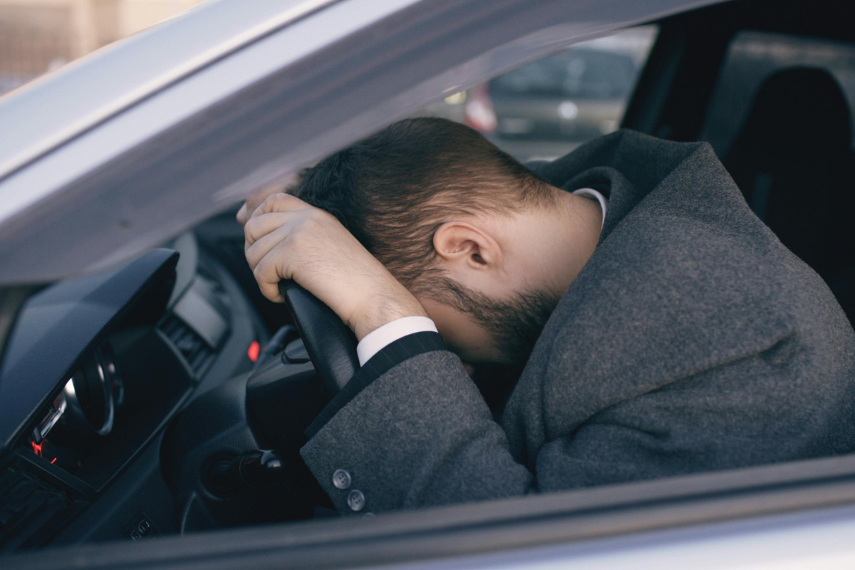Man slumped over steering wheel, looking exhausted.