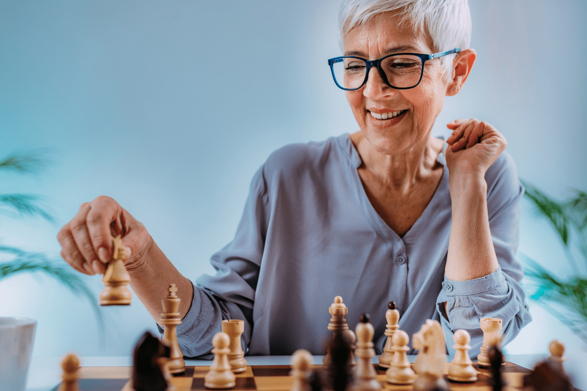 Smiling older woman with short white hair and glasses playing chess.