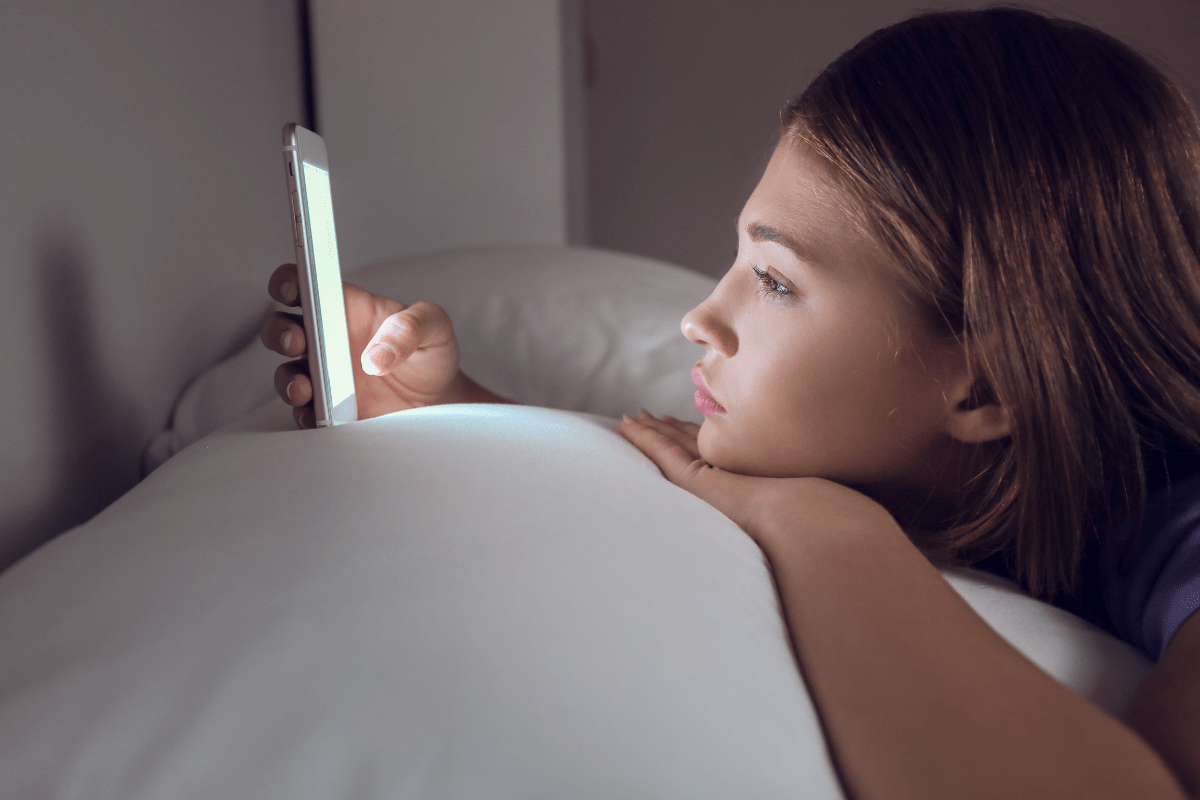 Young woman lying in bed, staring at her phone screen in the dark.