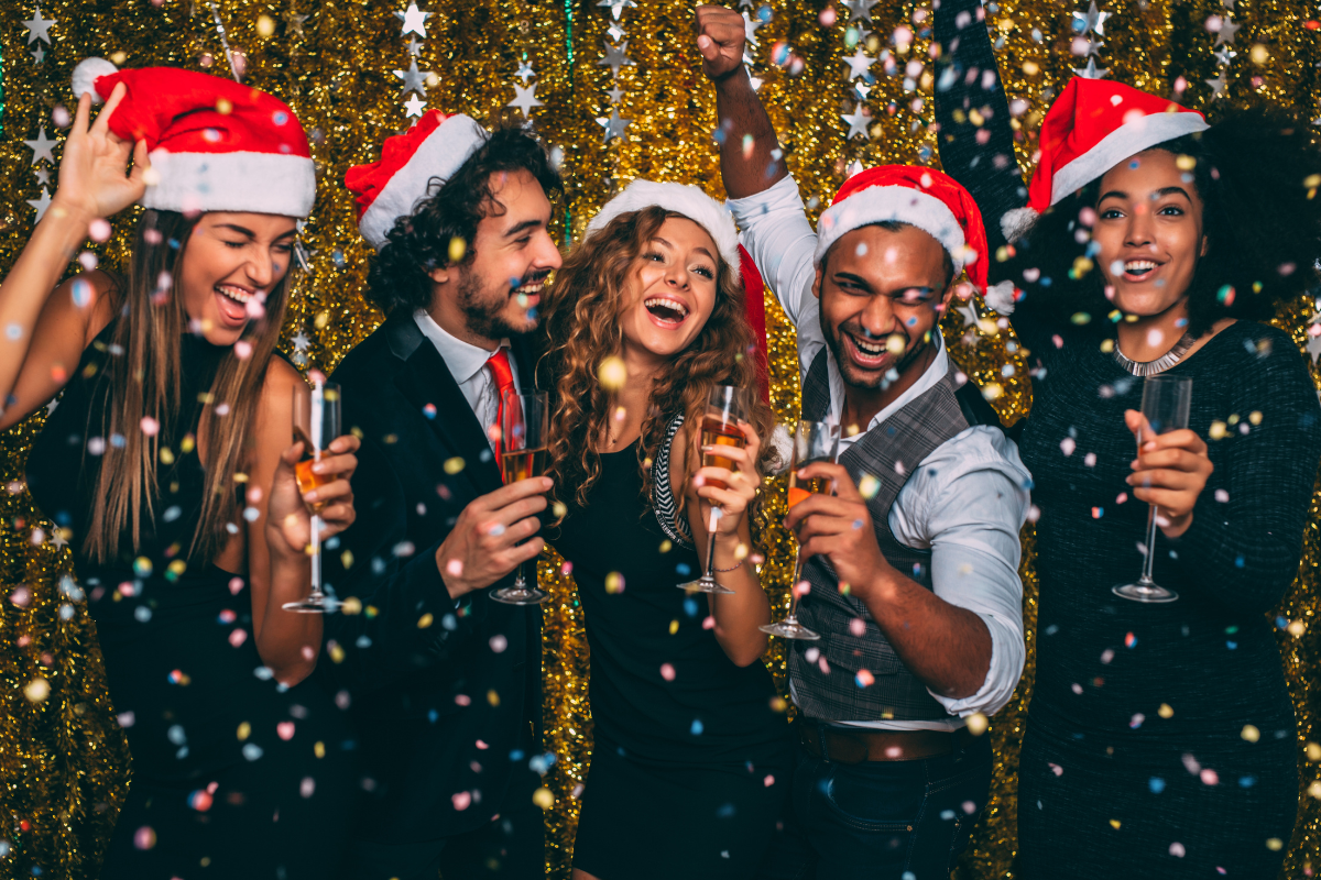Group of friends celebrating at festive party with champagne and Santa hats.