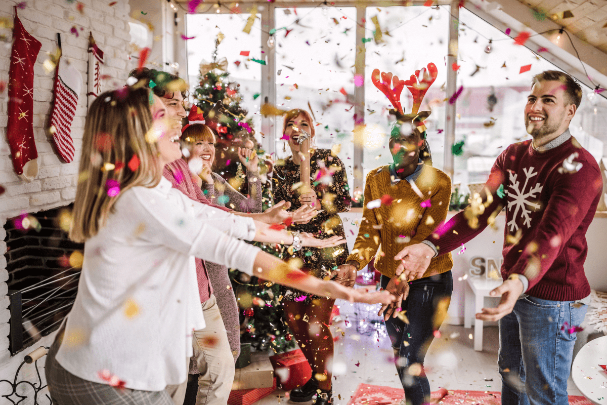 Group of friends celebrating indoors with confetti, festive decorations, and holiday cheer.