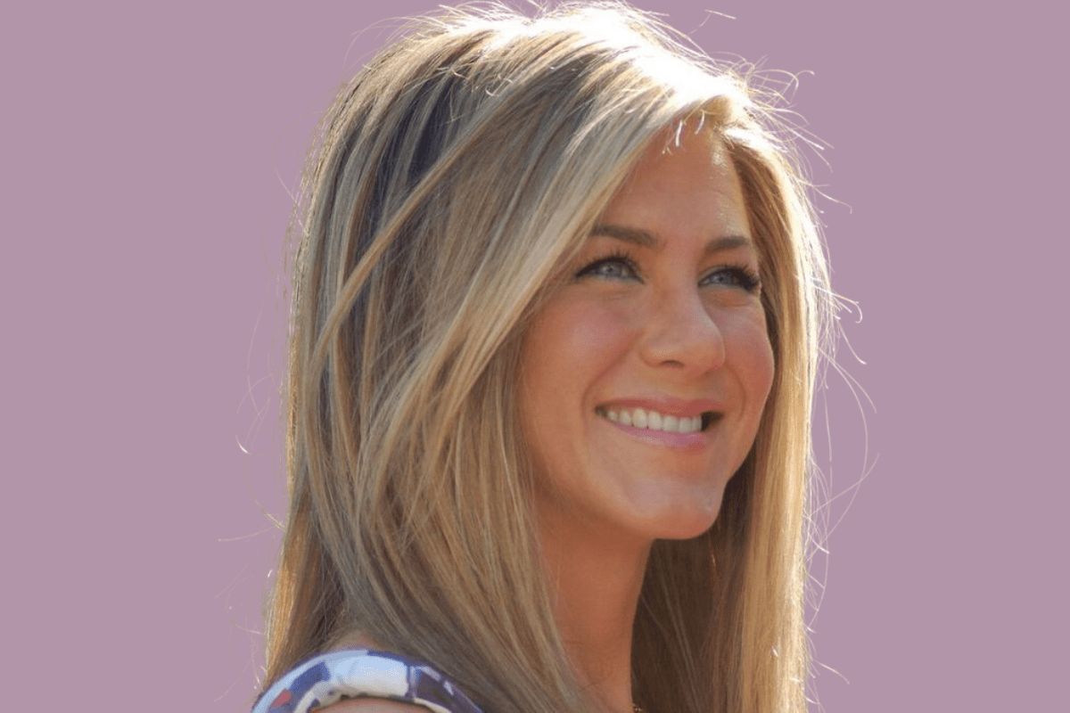 Smiling Jennifer Aniston with long blonde hair against a soft purple background.