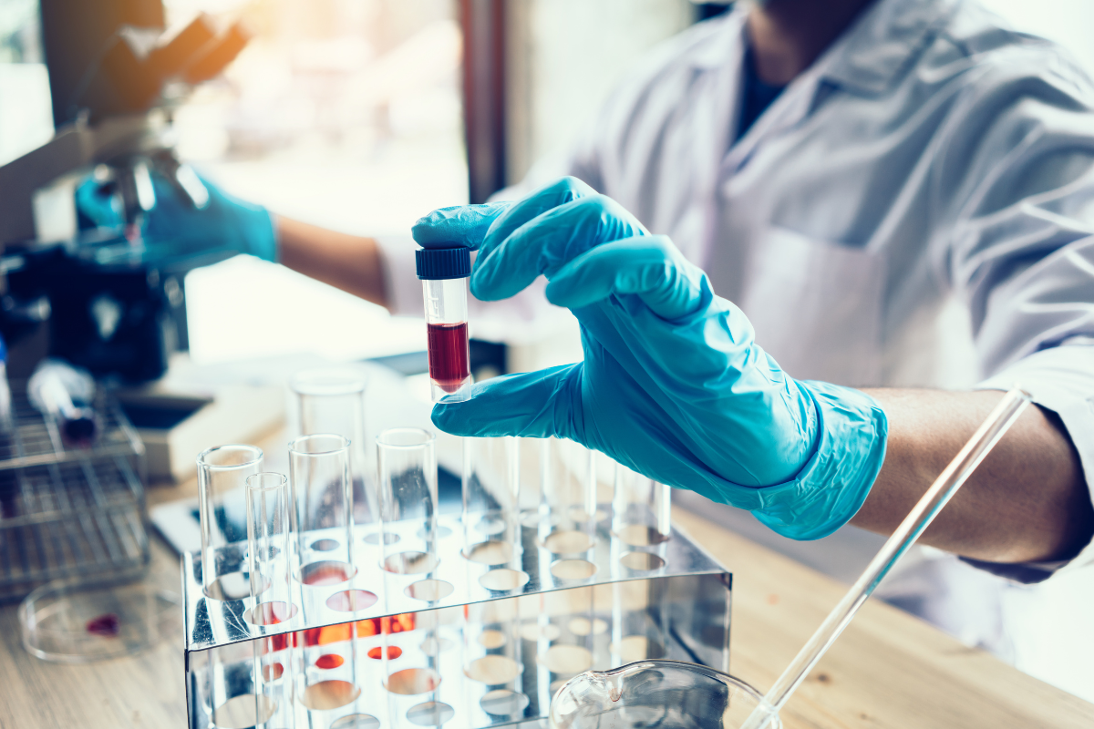 A scientist in a lab handling a test tube with a red liquid, surrounded by other test tubes.