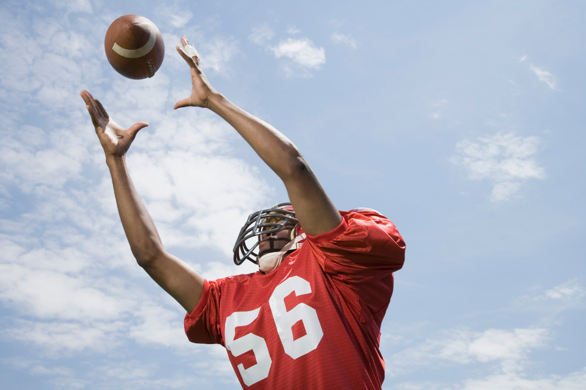 Athlete reaching to catch a football, showing quick reflexes and coordination.