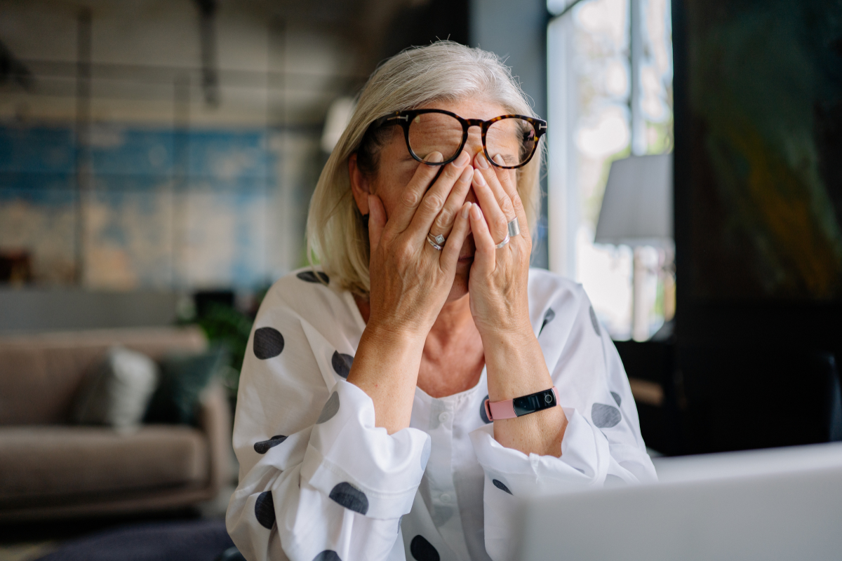 Older woman looking stressed and exhausted at her laptop.