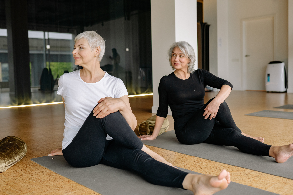 Two women over 40 stretching on yoga mats in a studio.