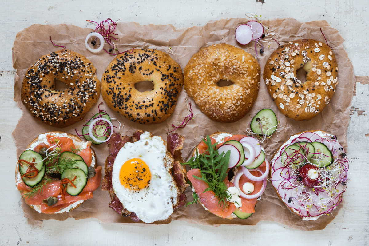 Bagels with toppings like salmon, egg, and veggies on parchment.